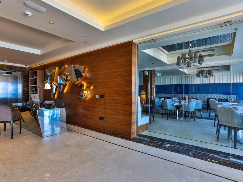 Moderner Hotelgang mit Sitzbereich und Glastür zum eleganten Restaurant mit blauen Stühlen.