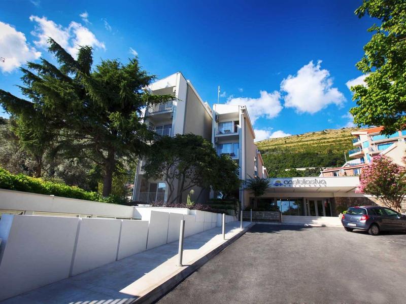 Moderner Gebäudekomplex mit weißen Wänden, breiter Einfahrt, grünen Bäumen und blauem Himmel.