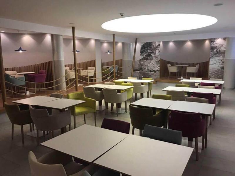 Moderner, heller Speisesaal mit weißen Tischen, gemischten Stühlen und betonter Deckenbeleuchtung.