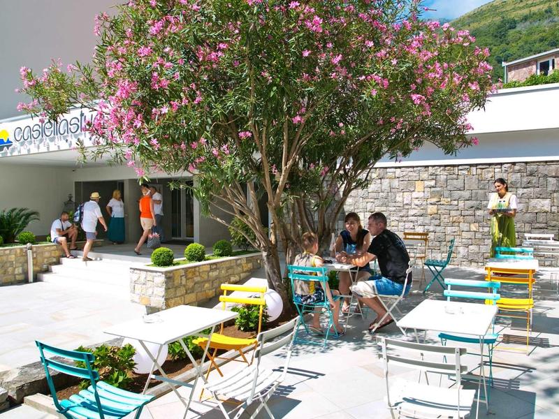 Bunt bemalte Stühle und Tische stehen unter einem blühenden Baum in einem sonnigen Innenhof.