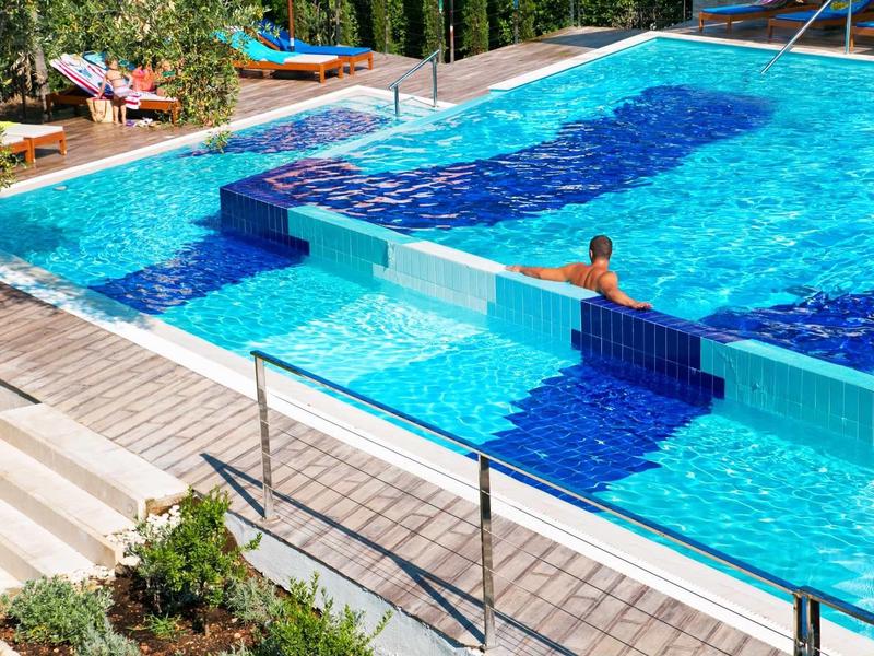 Klare blaue Schwimmbäder mit Treppen, Beckenrand und grünen Pflanzen rundherum.