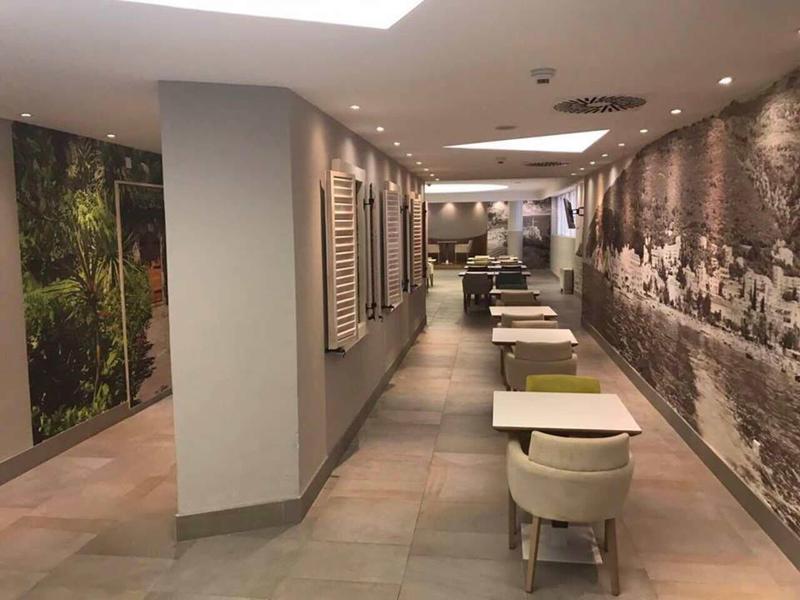 Moderner, langer Gang mit Sitzbereichen, grauen Fliesen und großen Wandbildern in neutralen Farben.