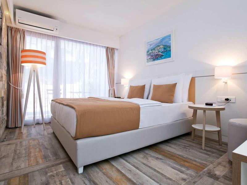 Modernes Schlafzimmer mit großem Bett, Holzboden, Stehlampe und Fenster mit weißen Vorhängen.