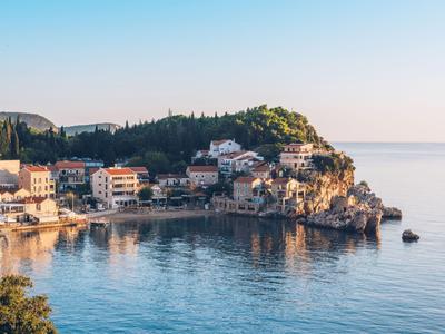 Picturesque coastal village with houses by the water and green hills by calm sea.
