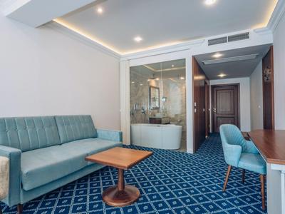 Moderne Hotellounge mit blauem Sofa, Tisch und Stuhl vor einem Badezimmer mit Badewanne