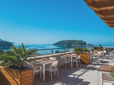 Terrasse mit Tischen und Stühlen, Blick auf das Meer und eine Insel unter klarem Himmel