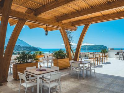 Covered terrace with wooden beams, tables, chairs, and view of sea and mountains.