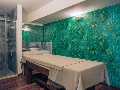 Behandlungsraum mit Massageliege und Glasdusche, tropische Tapete schafft entspannte Atmosphäre