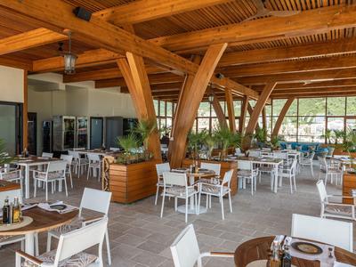 Helle, offene Terrasse mit weißen Stühlen und Holztischen unter Holzträgern.