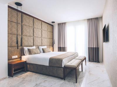 Modernes Hotelzimmer mit großem Bett, gepolstertem Kopfteil und Fenstervorhängen.