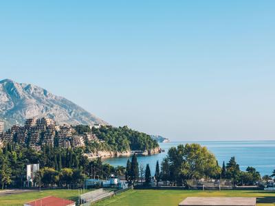 Blick auf Berge, Küste und Meer mit einigen Gebäuden und grünen Bäumen im Vordergrund.