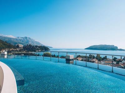 Infinity pool overlooking the sea and surrounding mountains on a sunny day.