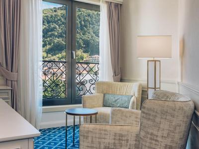 Gemütlicher Sitzbereich mit Sesseln, blauem Teppich und Blick auf grüne Hügel durch das Fenster.