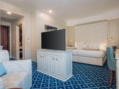 Modern eingerichtetes Hotelzimmer mit Fernseher, Bett und blauen Teppichboden.