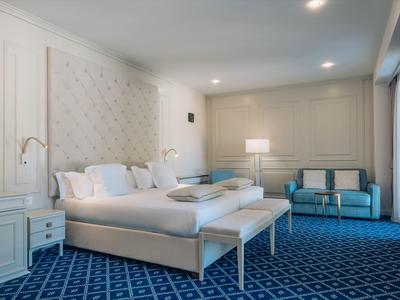 Elegantes Hotelzimmer mit großem Bett, blauer Teppich und Sitzbereich mit Sofas.