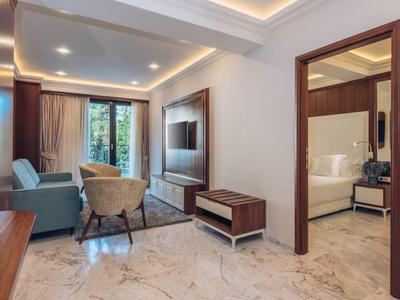 Moderner Hotelzimmer-Wohnbereich mit Sofa, Sesseln und Blick ins angrenzende Schlafzimmer.