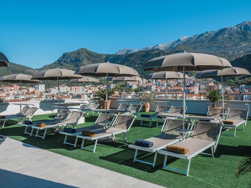 Liegestühle mit Sonnenschirmen auf Dachterrasse mit Berg- und Stadtblick