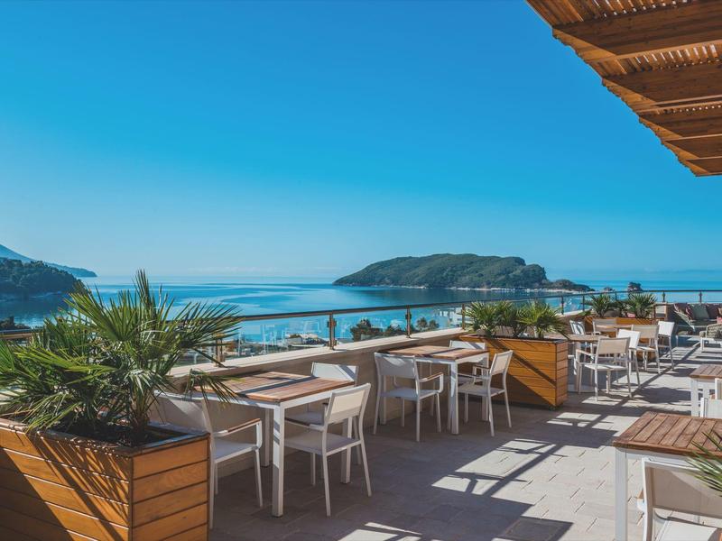 Terrasse mit Tischen und Stühlen, Blick auf das Meer und eine Insel unter klarem Himmel