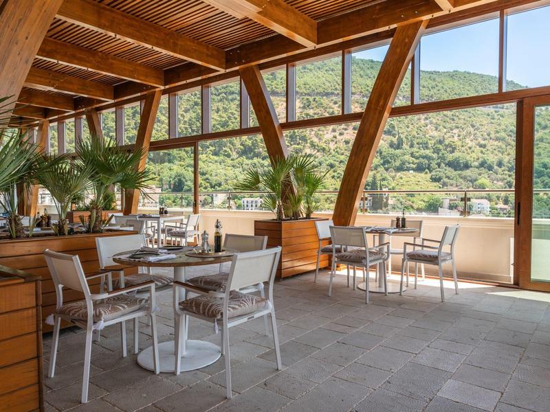 Überdachte Terrasse mit Tischen und Stühlen mit Blick auf bewaldete Hügel.