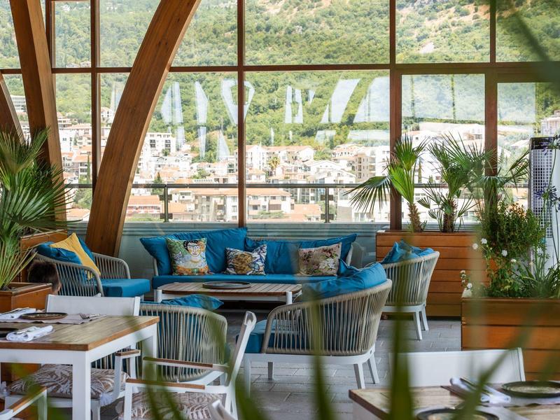 Helles Lounge-Bereich mit hölzernen Bögen, blauen Sofas und grünen Pflanzen mit Bergblick.