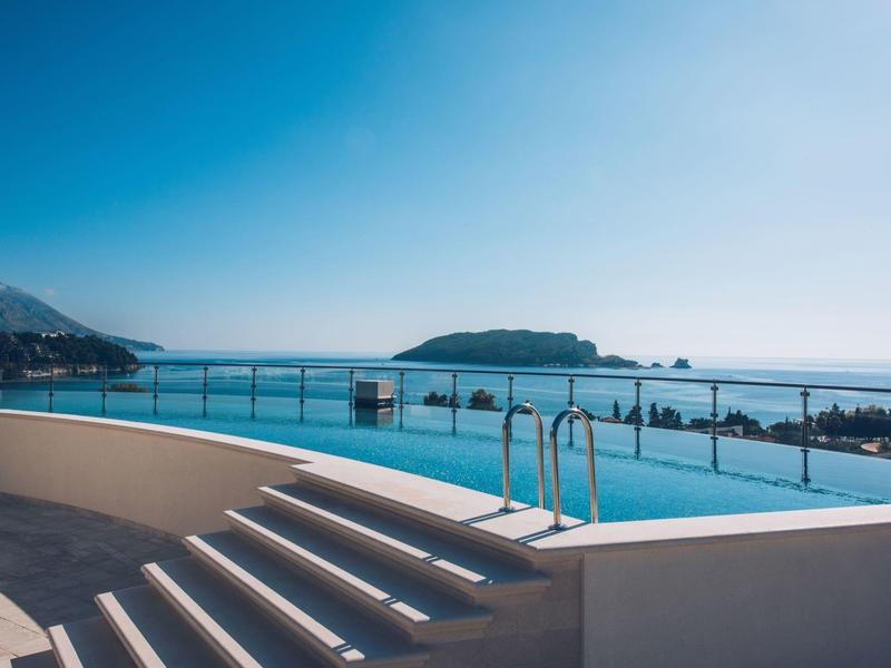 Gemütliche Sitzgruppe mit schwarzen Korbstühlen und Tischen auf einer Terrasse vor einem Hotel.