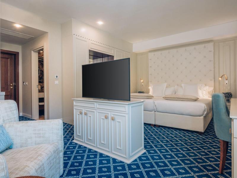 Modern eingerichtetes Hotelzimmer mit Fernseher, Bett und blauen Teppichboden.