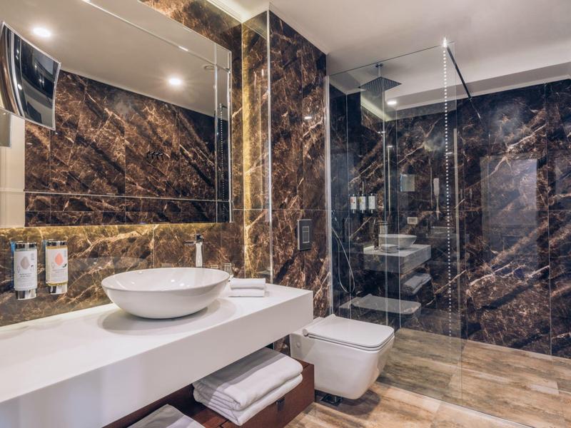 Elegantes Badezimmer mit dunklen Marmorwänden, freistehender Waschschale und ebenerdiger Dusche.