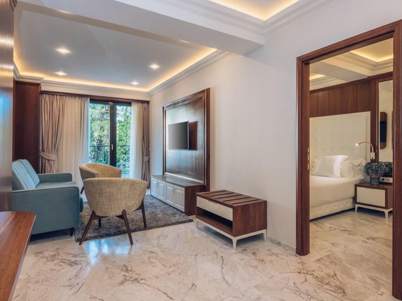 Moderner Hotelzimmer-Wohnbereich mit Sofa, Sesseln und Blick ins angrenzende Schlafzimmer.