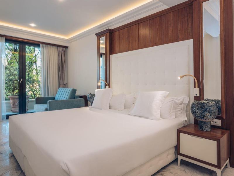 Modernes Hotelzimmer mit großem Bett, Sitzbereich und großen Fenstern mit Vorhängen.