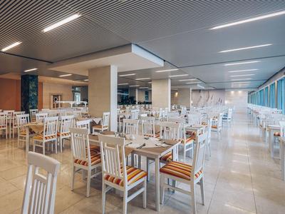 Duża jasna jadalnia z wieloma białymi krzesłami i drewnianymi stołami przy dużych oknach.