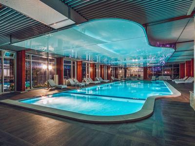 Nowoczesny basen kryty z oświetloną wodą i dużym przeszklonym dachem w hotelu.