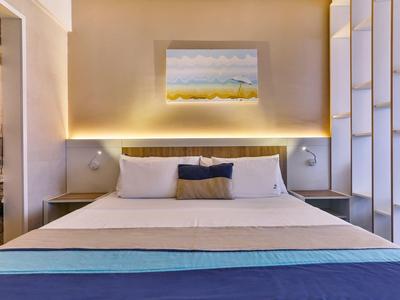 Nowoczesny pokój hotelowy z dużym łóżkiem, artystycznym obrazem i ciepłym oświetleniem.