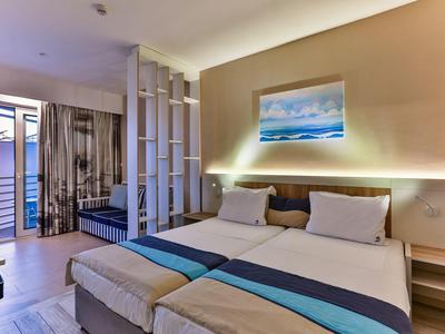 Nowoczesny pokój hotelowy z łóżkiem podwójnym, sofą i dostępem do balkonu z widokiem na morze.