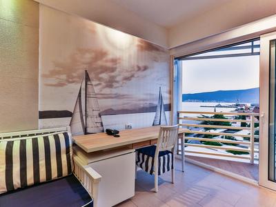 Balkon z krzesłem, stołem, widokiem na morze i obrazem żaglówki na ścianie w pokoju hotelowym.