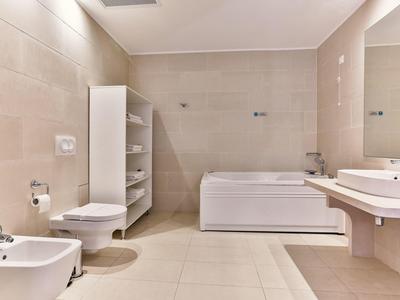 Nowoczesna łazienka z wanną, WC, bidetem, umywalką i regałem w jasnych kolorach.