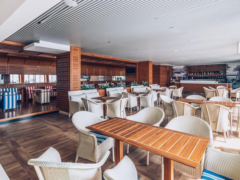 Jasna restauracja z drewnianymi stołami i białymi krzesłami w stylowym wnętrzu.