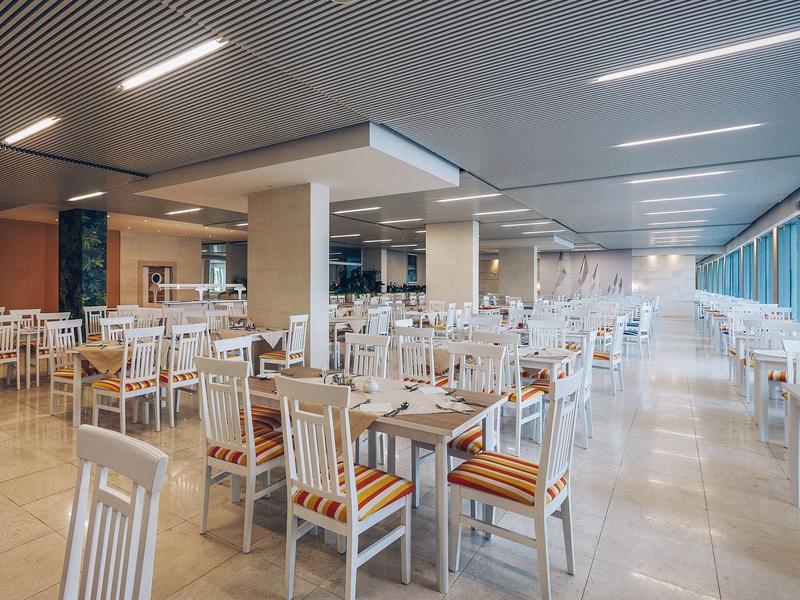 Duża jasna jadalnia z wieloma białymi krzesłami i drewnianymi stołami przy dużych oknach.