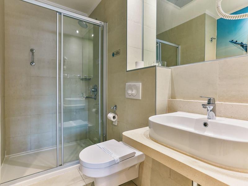 Nowoczesna łazienka z kabiną prysznicową, toaletą wiszącą i umywalką w neutralnych kolorach.