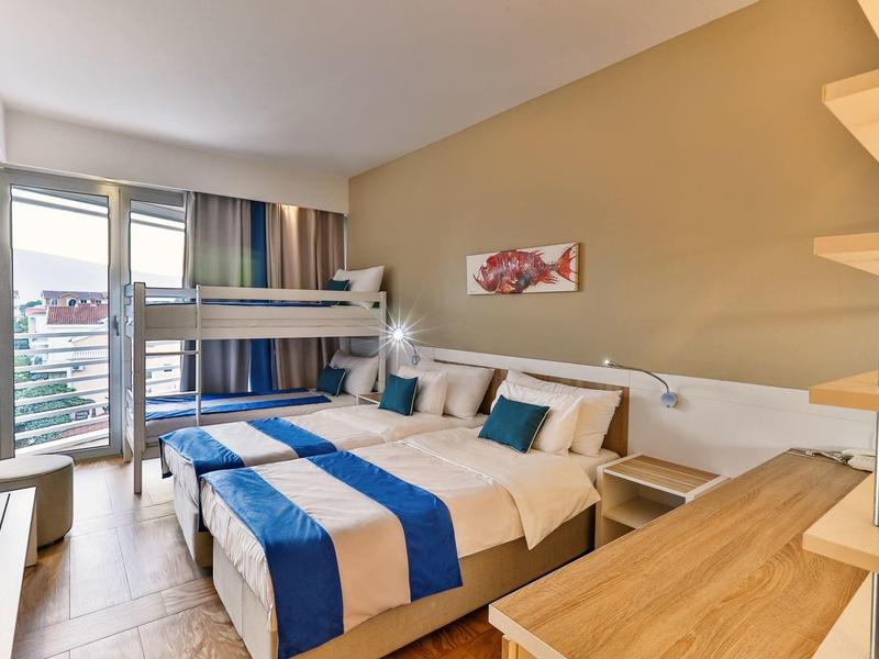 Jasny pokój hotelowy z łóżkiem podwójnym, łóżkiem piętrowym i balkonem z widokiem na miasto.