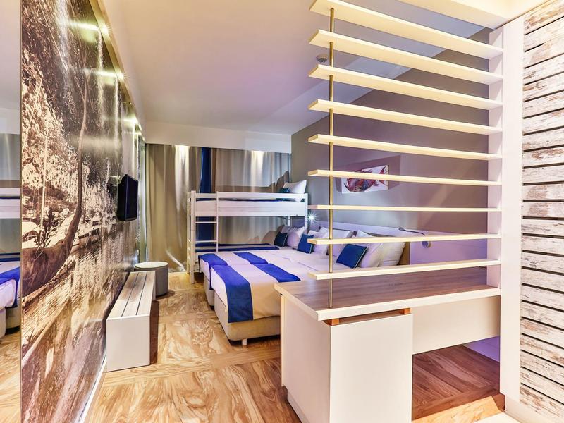 Nowoczesny pokój hotelowy z łóżkiem podwójnym, osobną częścią do spania i drewnianą podłogą.