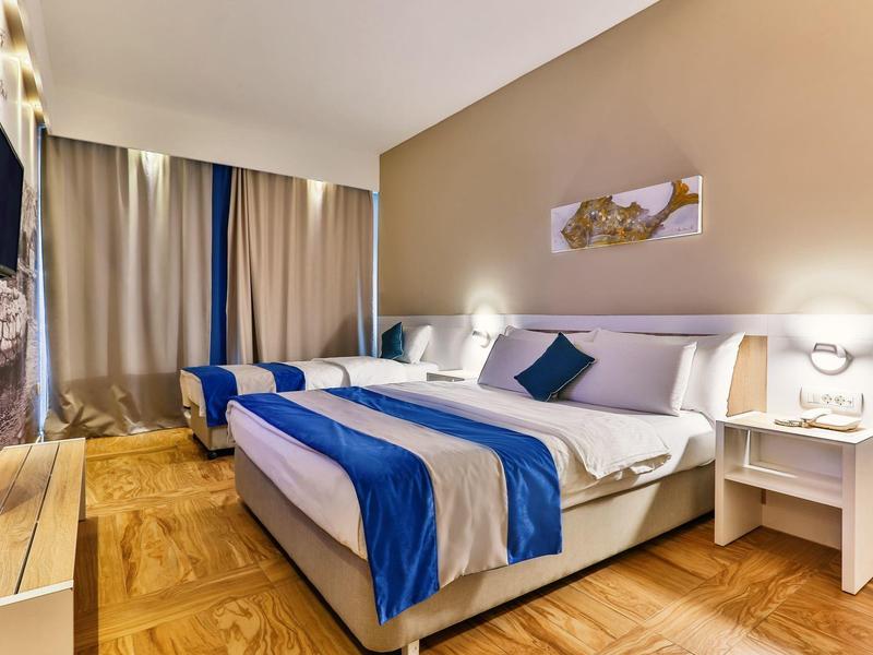 Nowoczesny pokój hotelowy z łóżkiem podwójnym, niebieskimi akcentami i drewnianą podłogą.