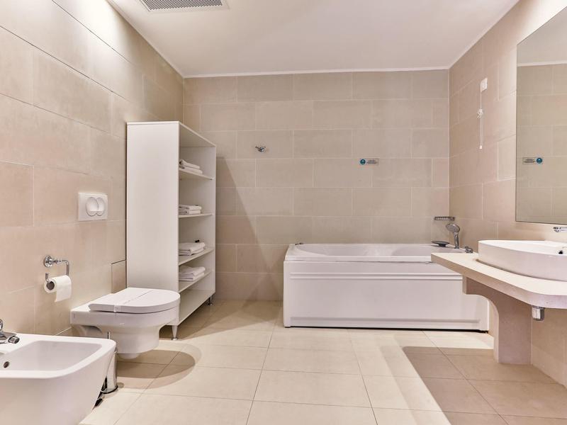 Nowoczesna łazienka z wanną, WC, bidetem, umywalką i regałem w jasnych kolorach.