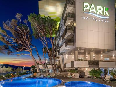 Hotel mit beleuchtetem Pool und Abendhimmel, flankiert von Bäumen und moderner Architektur.