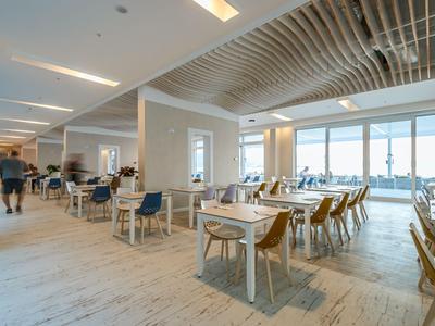 Helles Restaurant mit Holzmöbeln und großen Fenstern mit Meerblick in einem Hotel.