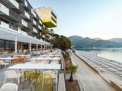 Terrasse eines Hotels mit Tischen und Stühlen mit Blick auf Strand und Meer unter klarem Himmel.