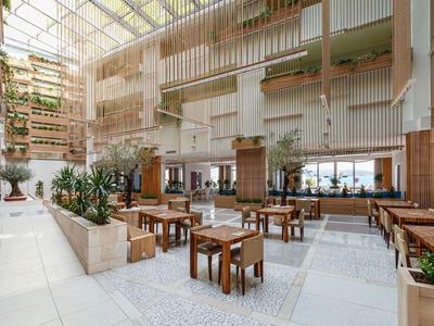 Heller, offener Hotellobby-Bereich mit natürlichem Licht, Holzstühlen und grünen Pflanzen.