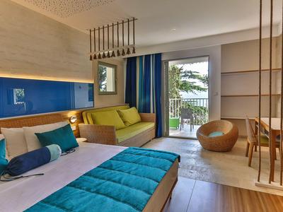 Modernes Hotelzimmer mit blauem Bett, gelbem Sofa und Blick auf einen Balkon mit Meerblick.