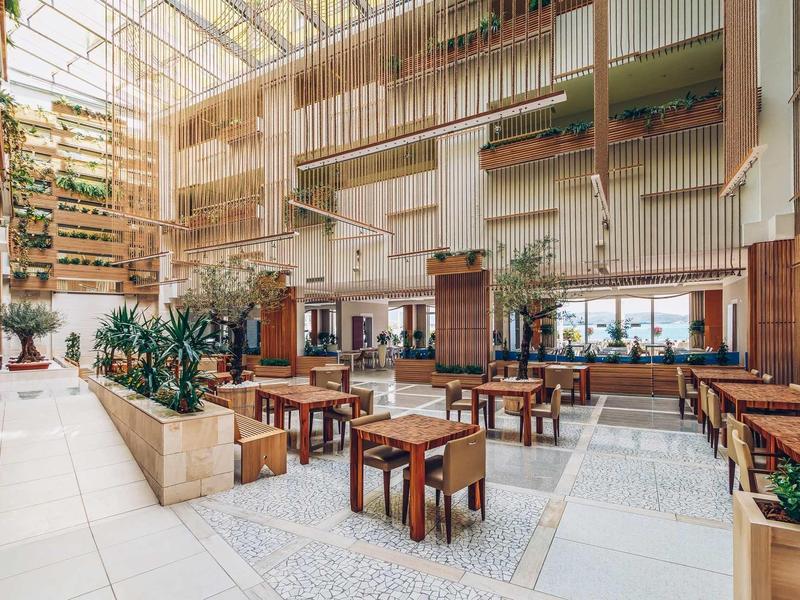 Bright atrium with wooden furniture, plants, and natural light in a modern hotel.