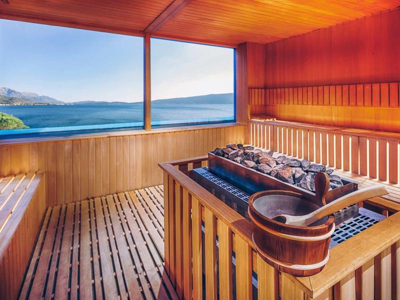 Wood-paneled sauna with large window overlooking the sea.