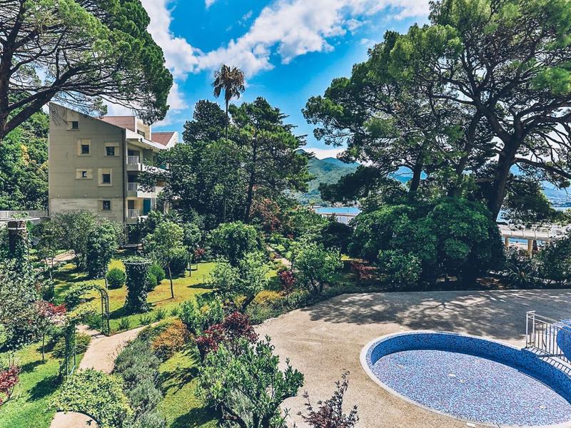 Garden with pool and large trees near a multi-story building under a blue sky.
